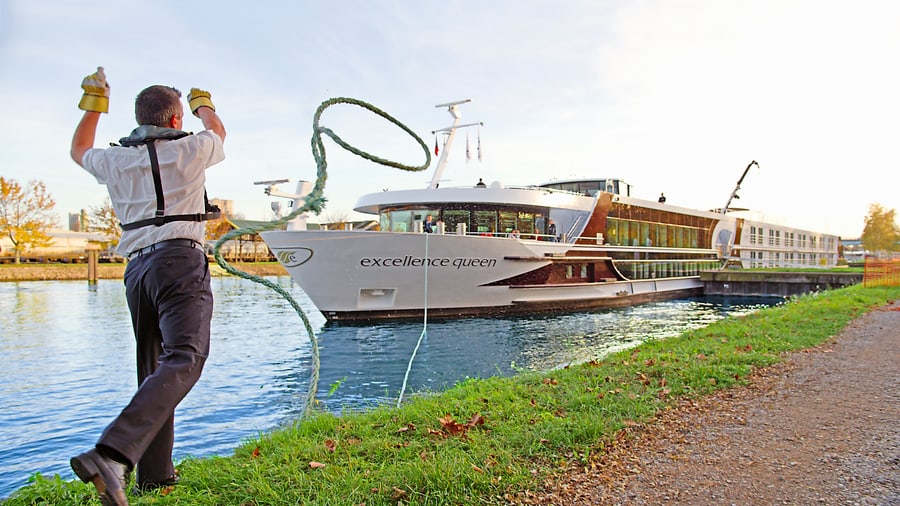 Mann wirft Seil zu Kreuzfahrtschiff Excellence Queen am Fluss.