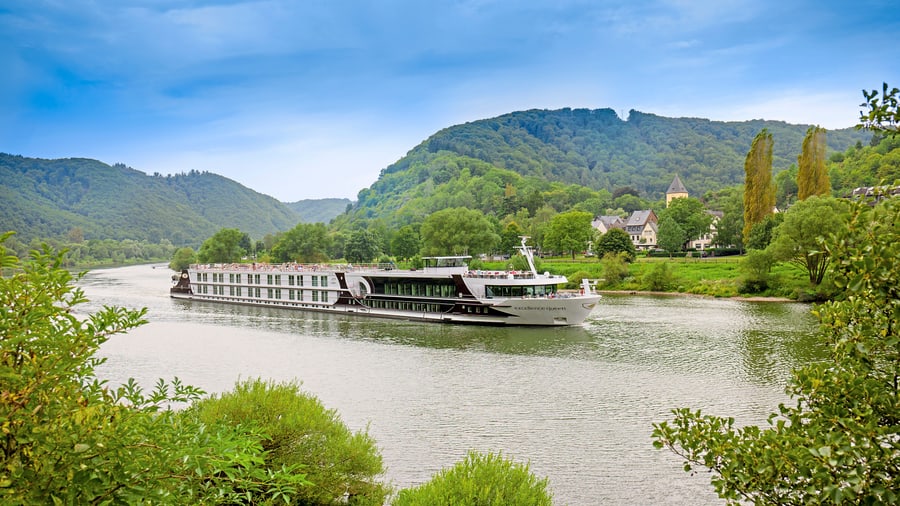 Flusskreuzfahrtschiff auf dem Fluss vor bewaldeten Hügeln.