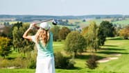 Frau schwingt Golfschläger auf grünem Golfplatz.