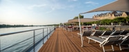 Deck eines Kreuzfahrtschiffs mit Liegestühlen und Sonnensegeln am Flussufer.