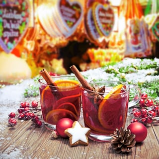 herrlicher-gluehwein.jpg Zwei Glühweintassen mit Zimtstangen und Orangen.