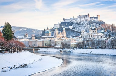 Winteransicht der verschneiten Stadt Salzburg mit Festung, Fluss und Gebäuden.