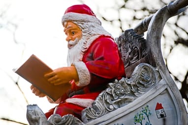 Weihnachtsmannfigur in Schlitten liest Buch.
