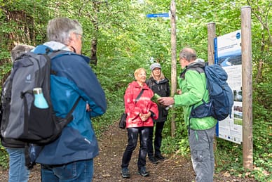 Gruppe von Wanderern steht im Wald vor einer Informationstafel.