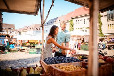 Zwei Personen stehen an einem Obststand auf einem Markt.