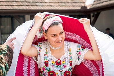 Frau in bunter traditioneller Tracht mit gestickten Mustern und Kopfschmuck.