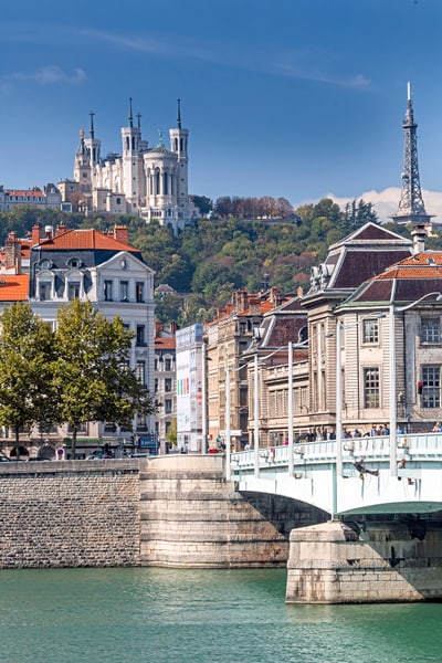 Stadtansicht mit Fluss, Brücke und Hügel mit Kirche im Hintergrund.