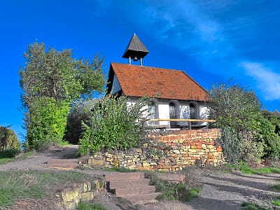 Kleines Gebäude mit rotem Dach und Glockenturm, umgeben von Bäumen.
