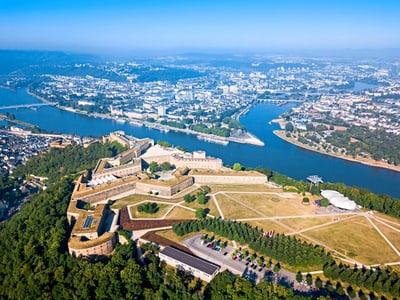 Luftaufnahme einer Festung am Fluss mit Stadt im Hintergrund.