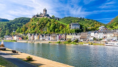 Schloss auf Hügel über Fluss und bunte Häuserreihe.