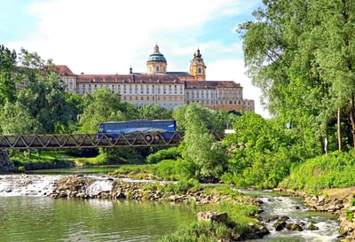 Majestätisches Gebäude hinter bewaldetem Fluss und Brücke.
