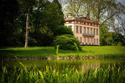 Grosses beige Gebäude in einem parkähnlichen Garten mit einem Teich im Vordergrund.