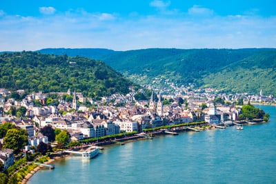 Luftaufnahme einer Stadt am Fluss mit Hügeln im Hintergrund.