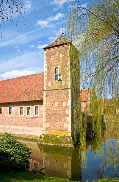 Mittelalterlicher Turm neben einem Wassergraben, umgeben von Bäumen.