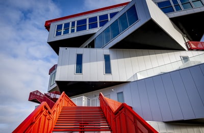 Modernes Gebäude mit roten Treppen und kantiger Architektur gegen blauen Himmel.