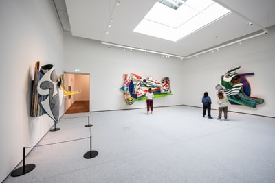 Galerie mit abstrakten Wandkunstwerken und drei Personen, die sie betrachten.