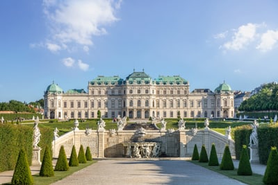 Barocker Palast mit Garten und Statuen bei blauem Himmel.
