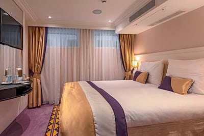 Hotelzimmer mit Doppelbett, Vorhängen und Fernseher.