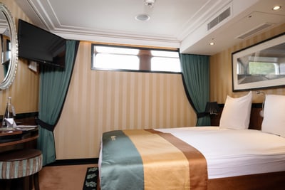 Hotelzimmer mit Doppelbett, Spiegel, Fernseher und Fenster.