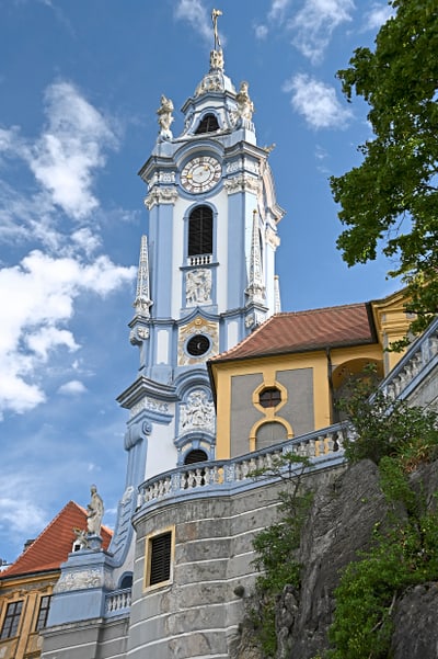 Barockkirchturm mit blauem Himmel und Wolken.