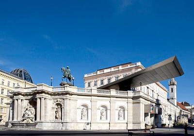 Historisches Gebäude mit Reiterstatue und moderner Dachstruktur unter klarem Himmel.