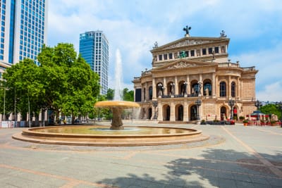 Opernhaus mit Brunnen und Hochhäusern im Hintergrund bei Tag.