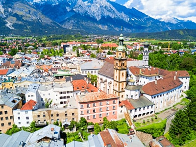 Luftaufnahme einer Stadt mit Kirche und Bergen im Hintergrund.