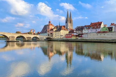 Flussblick auf mittelalterliche Stadt mit Brücke und Kirchtürmen.