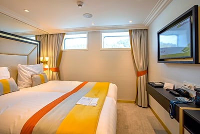 Modernes Schlafzimmer mit Doppelbett, Vorhängen und Fernseher.