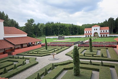 Rekonstruktion eines römischen Landguts mit gepflegten Hecken und Gebäuden, umgeben von Wald.
