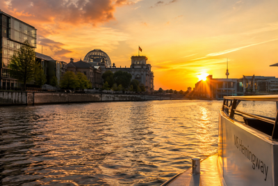 Sonnenuntergang über einem Fluss mit Gebäuden am Ufer und einem Boot im Vordergrund.