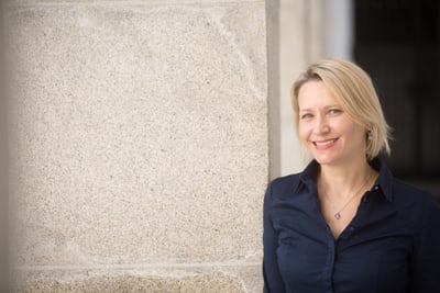 Frau mit blondem Haar lächelt vor einer Steinwand.