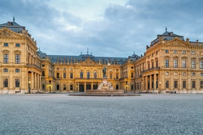 Barockpalast mit Statue und gepflastertem Platz.