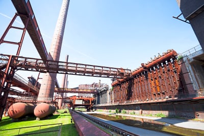 Historische Industrielandschaft mit Schornstein und Stahlstrukturen.
