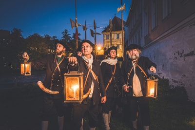 Vier Personen in historischer Kleidung halten Laternen bei Nacht.