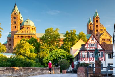 Eine Person auf einem Weg vor einer grossen Kirche und Fachwerkhäusern bei blauem Himmel.