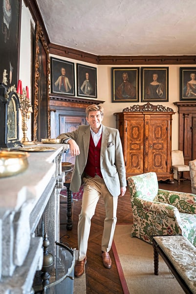 Mann in historischem Raum mit Gemälden und Holzmöbeln.