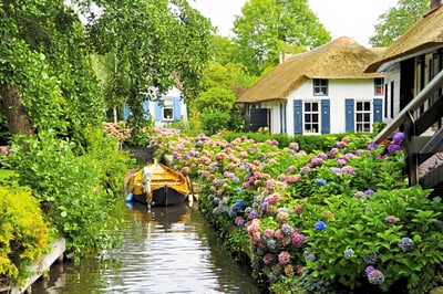 Blumen gesäumter Kanal mit Boot und Strohdachhäusern.