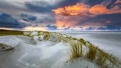Sanddünen an der Küste bei Sonnenuntergang mit dramatischem Himmel.