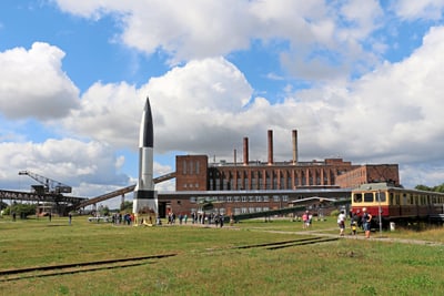 Fabrikgebäude mit Rakete und historischem Zug im Vordergrund.