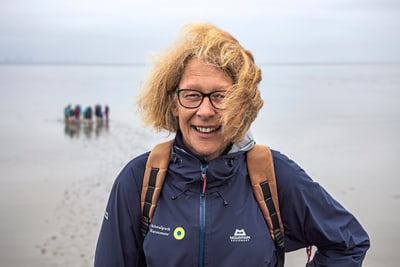 Lächelnde Person am Strand mit Wandergruppe im Hintergrund.