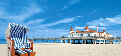 Strandkorb vor Seebrücke und Gebäude am Sandstrand.
