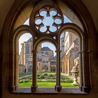Blick aus einem gotischen Fenster auf einen historischen Innenhof mit Garten.