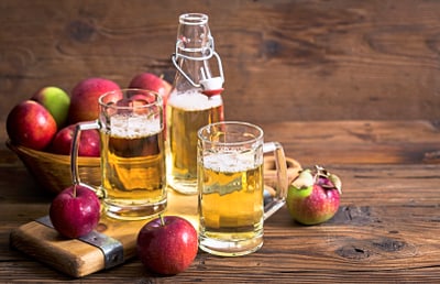 Frische Äpfel und Apfelwein in Gläsern auf Holztisch.