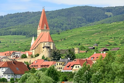 Historisches Dorf mit Kirche in hügeliger Landschaft.