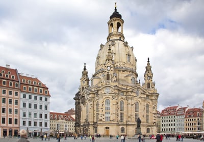 Historisches Gebäude auf einem Platz mit umliegenden Gebäuden und Menschen.