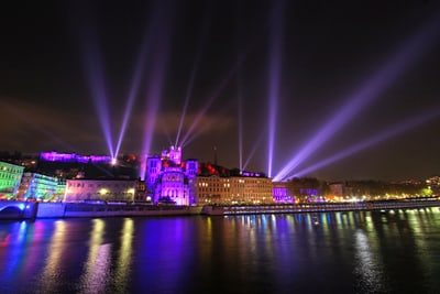 Nachts beleuchtete Gebäude mit Lichtsäulen am Fluss.