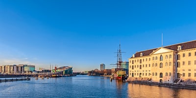Wasserblick auf Gebäude und Schiff unter blauem Himmel.