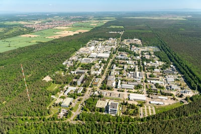Luftaufnahme eines grossen Industriekomplexes inmitten eines Waldes mit weitläufiger Landschaft im Hintergrund.