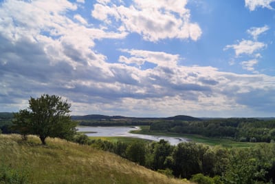 Landschaft mit Fluss, Hügeln und Wolkenhimmel.
